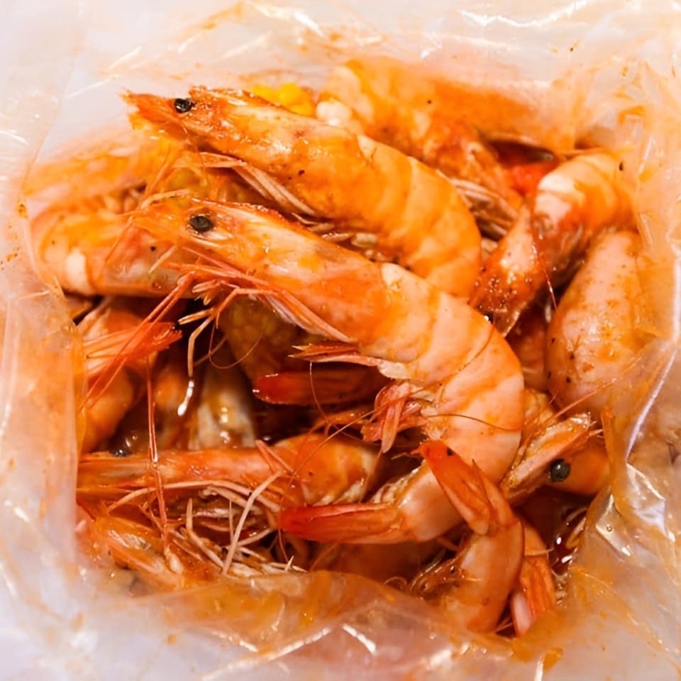 Close-up of seasoned shrimp in a clear plastic bag, glistening with sauce.