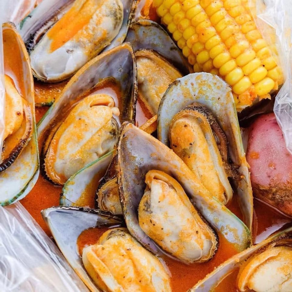 Steamed mussels in a spicy red sauce with corn on the cob and a potato.