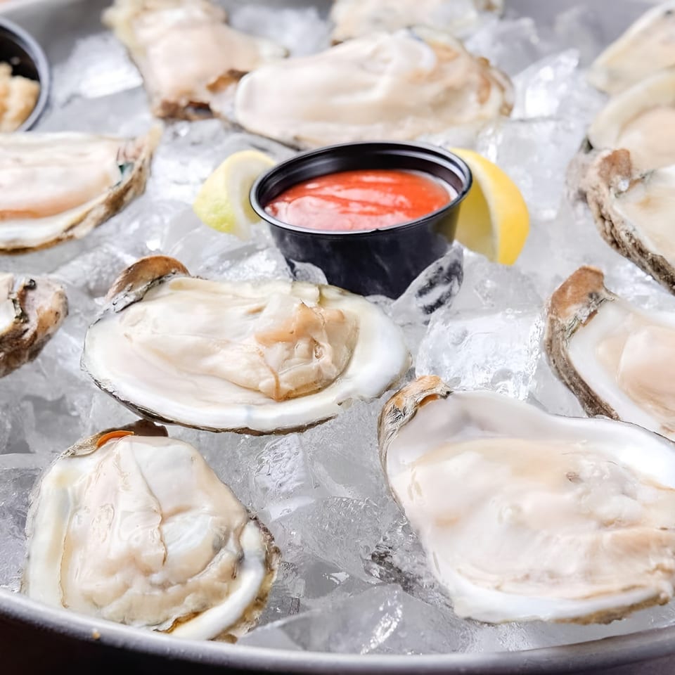 Fresh oysters on a bed of ice with cocktail sauce and lemon wedges.