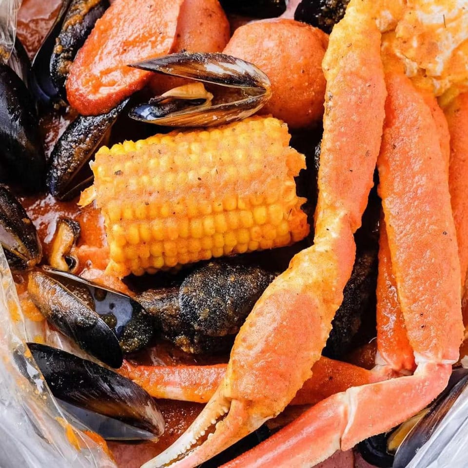 Close-up of a seafood boil with mussels, crab legs, corn on the cob, and potatoes.
