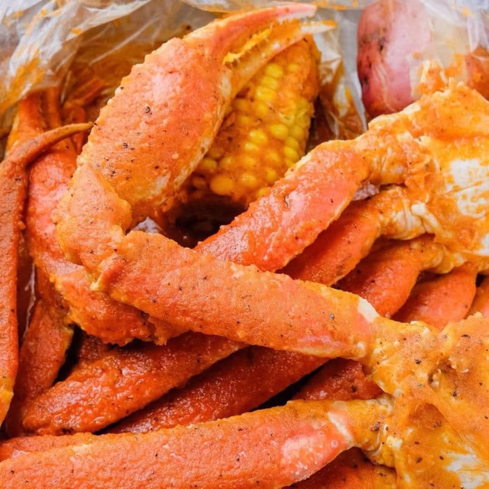 Close-up of seasoned crab legs, corn on the cob, and a potato in a plastic bag.