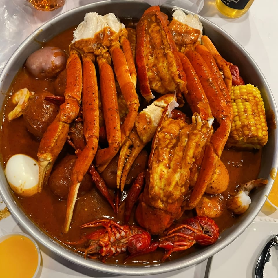 A large metal bowl filled with a seafood boil of crab legs, lobster, crawfish, corn, potatoes, and egg.