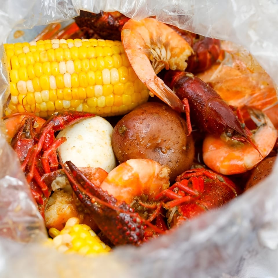 Boiled crawfish, shrimp, corn on the cob, and potatoes in a clear plastic bag.
